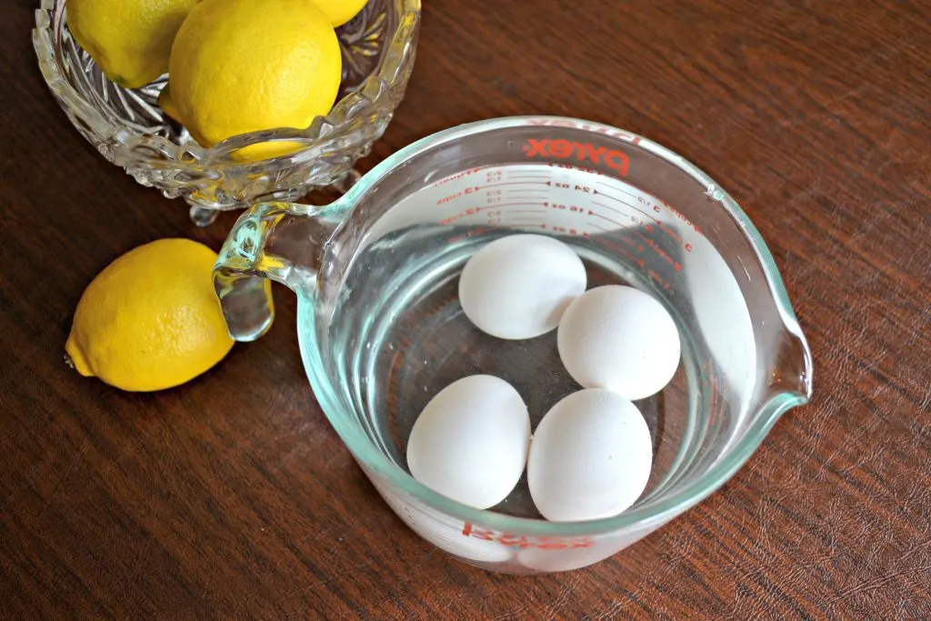 Four eggs in water next to a bowl of lemons