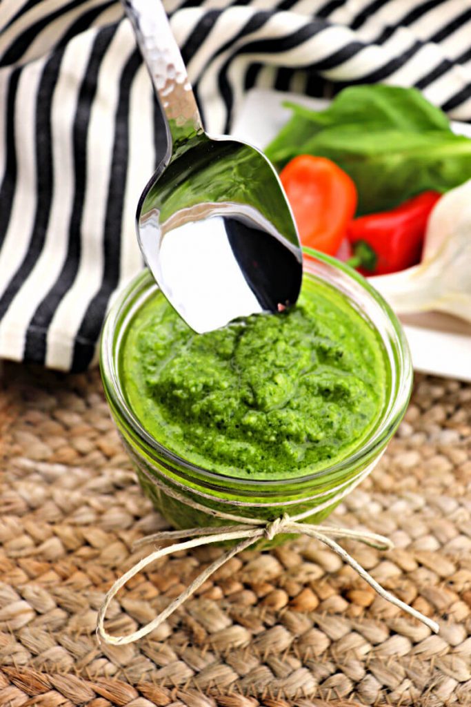 Spoon dips into a jar of basil keto pesto sauce. #ketorecipes #italianketo