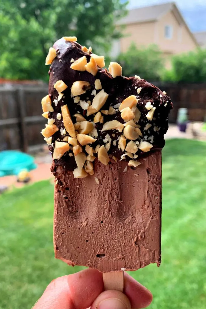 Bite out of a keto chocolate ice cream bar dipped in chocolate and peanuts.