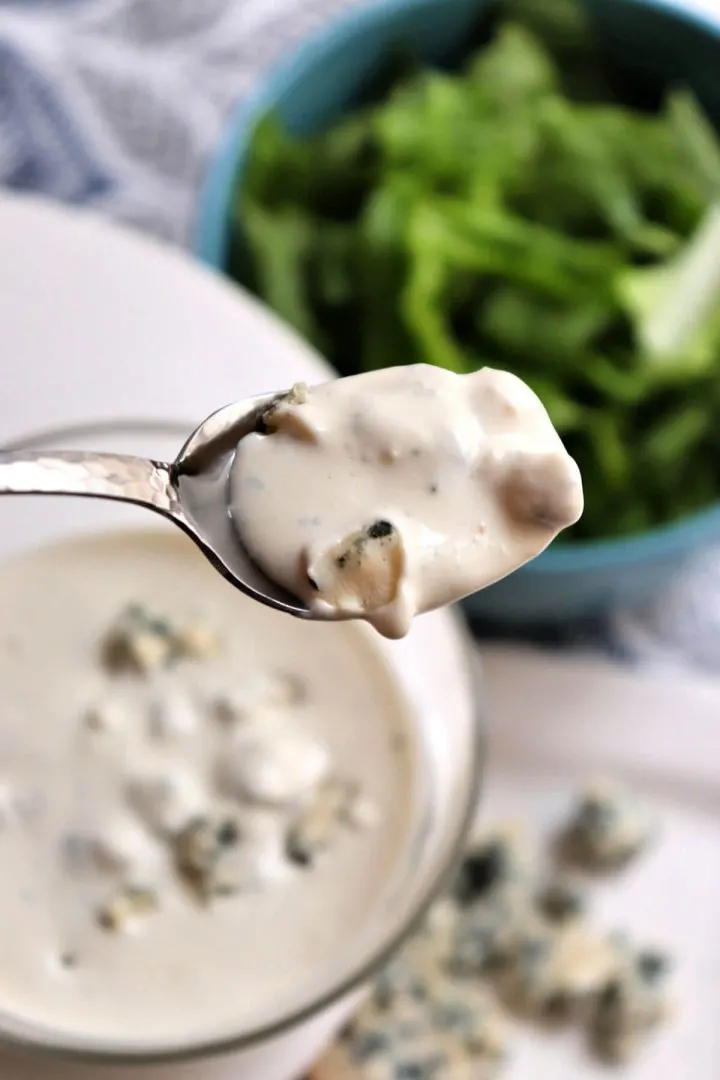 Spoon of keto blue cheese dressing with a bowl and lettuce in the background.