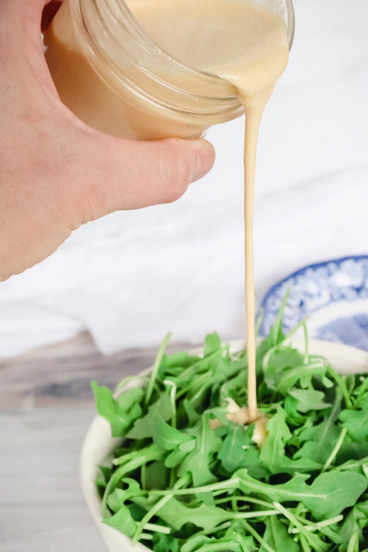 Pouring keto tahini dressing on arugula