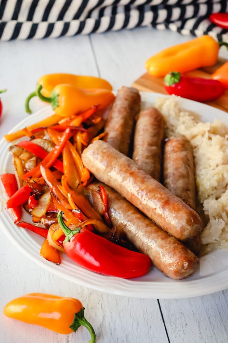 Brats in air fryer cooked on a plate with peppers and sauerkraut