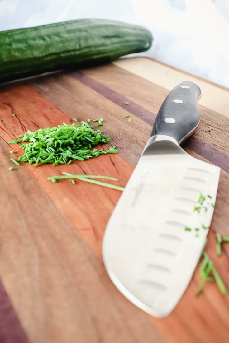 Cucumber, chopped chives, and a knife on a cutting board