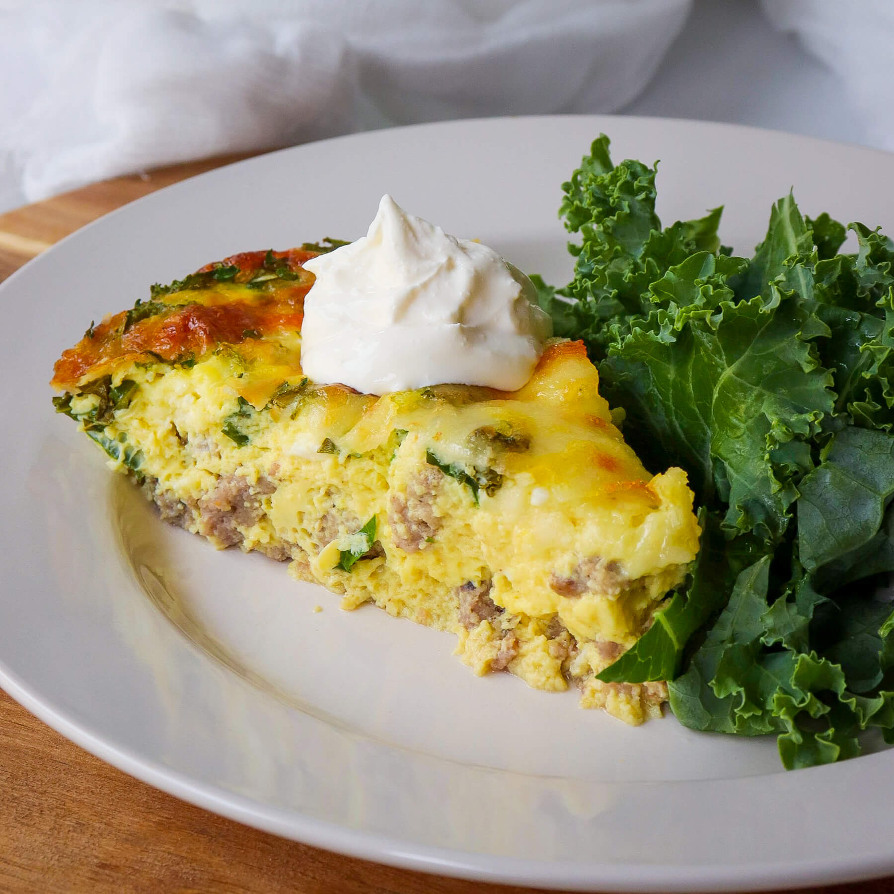 Piece of keto quiche, sausage and kale on a white plate