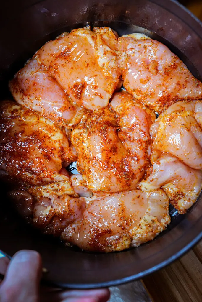 Raw chicken thighs with spices in the air fryer basket to cook