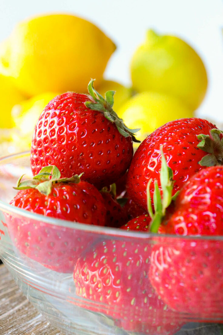 A bowl of strawberries with lemons in the background