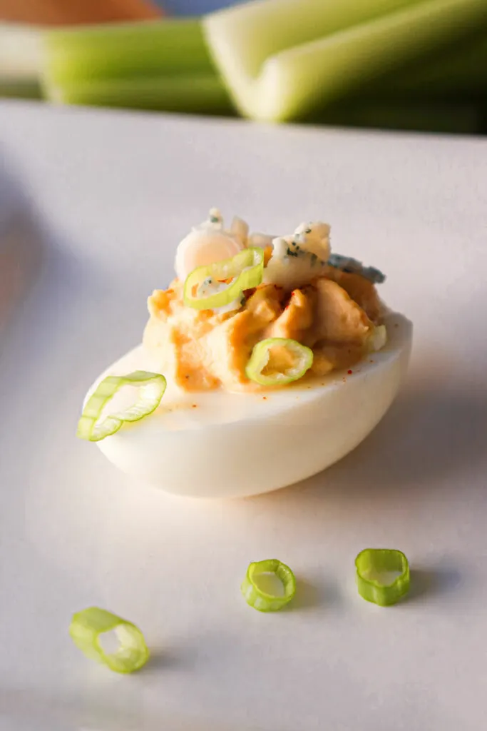 One deviled egg sitting on a white plate with celery in the background