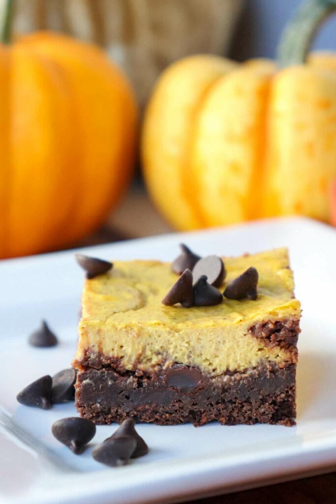 One keto pumpkin brownie on a white plate with pumpkins in the background