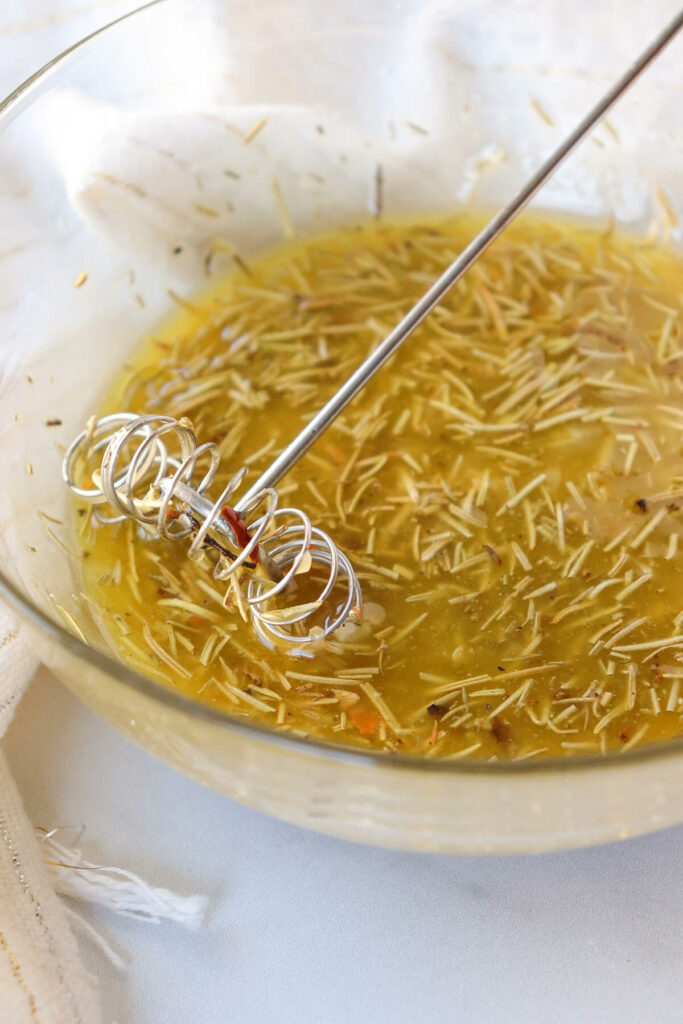 A clear glass bowl with the Greek marinade and a small whisk sitting in the bowl