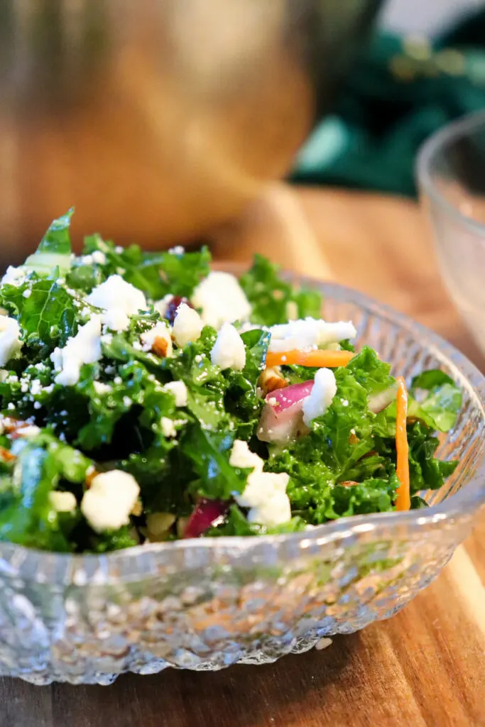 A glass bowl of keto kale salad on wood