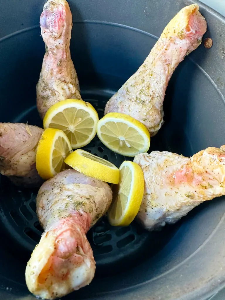 Overhead view of air fryer basket with raw chicken legs ready to cook