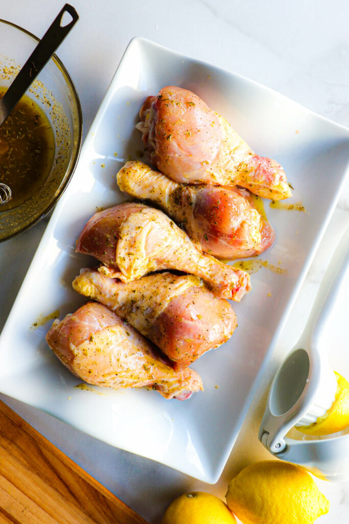 Raw chicken drumsticks ready to cook on a white platter