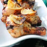 A white platter of air fryer chicken legs with lemon slices