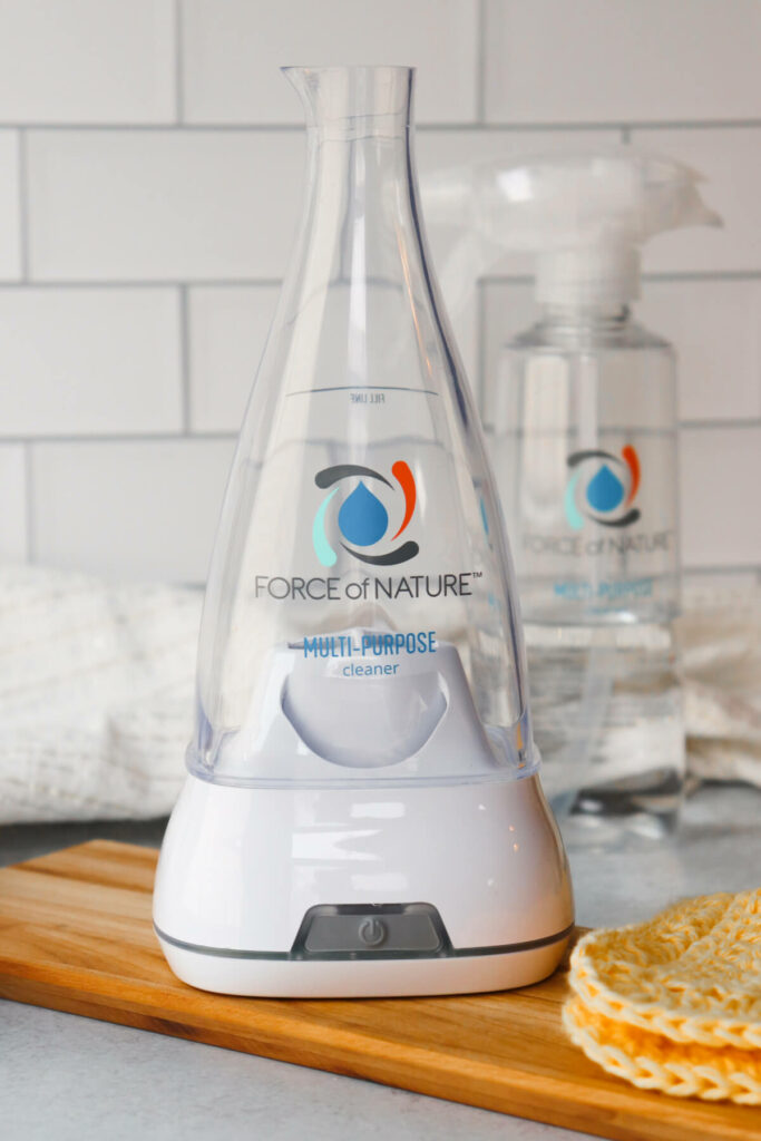 A view of the Force of Nature cleaner maker appliance with a spray bottle in the background.