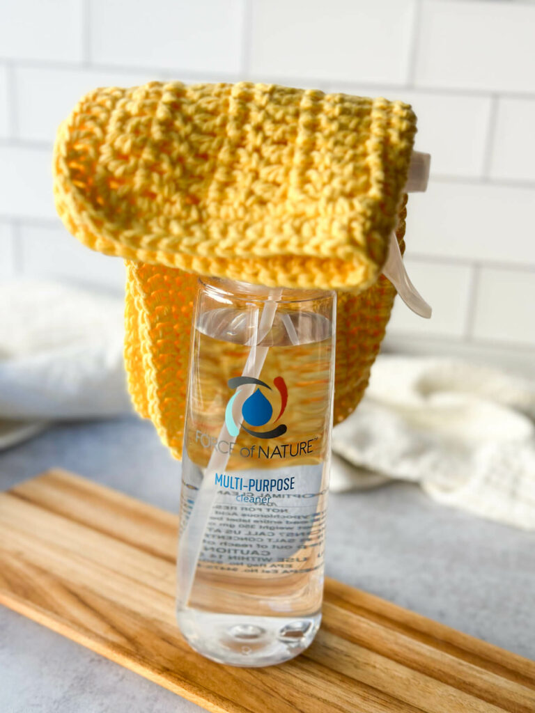 A yellow crocheted cleaning cloth on top of the Force of Nature cleaner spray bottle.