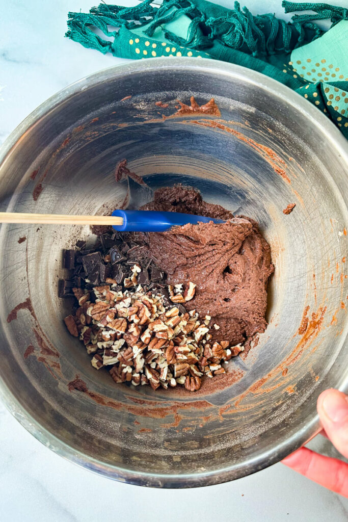 Overhead view of a bowl with a spatula folding in pecans and chopped chocolate