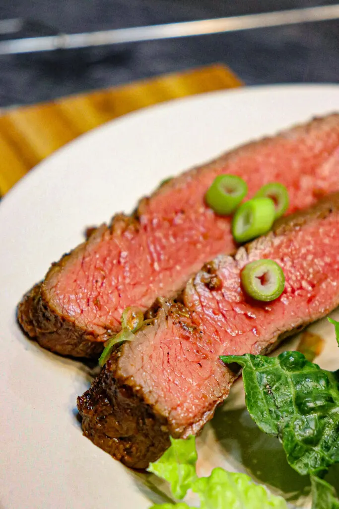 2 slices of keto flank steak on a white plate with a salad