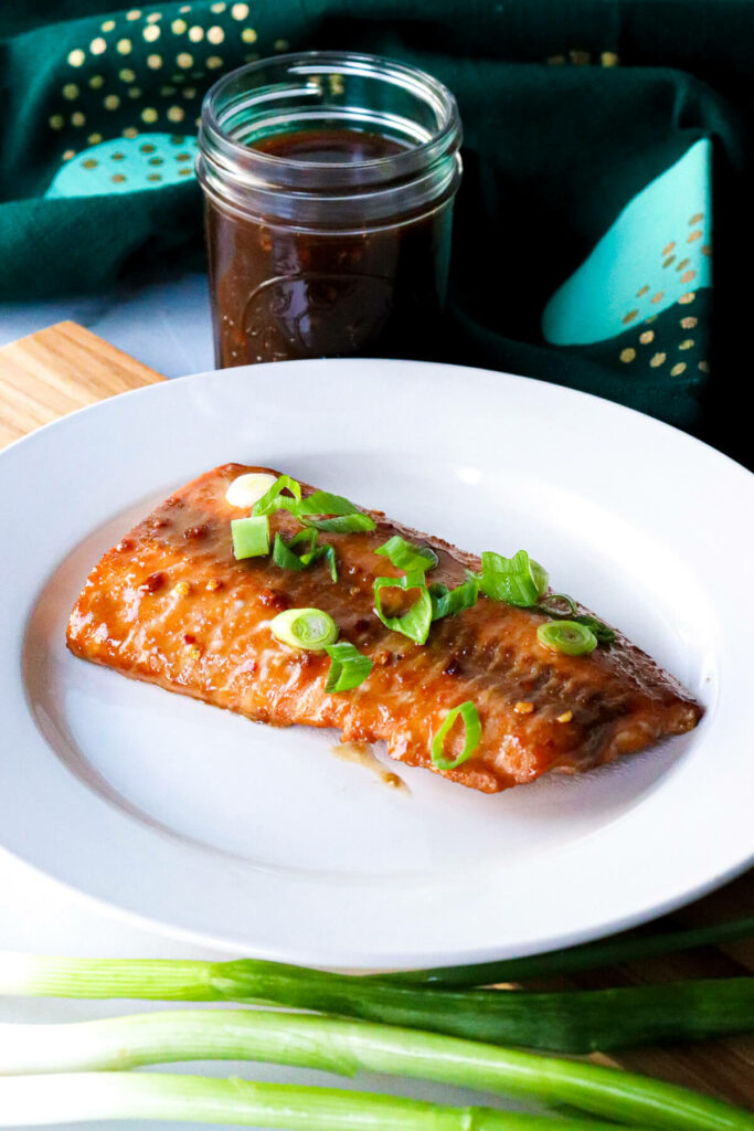 A serving of air fryer teriyaki salmon on a white plate with green onions on top