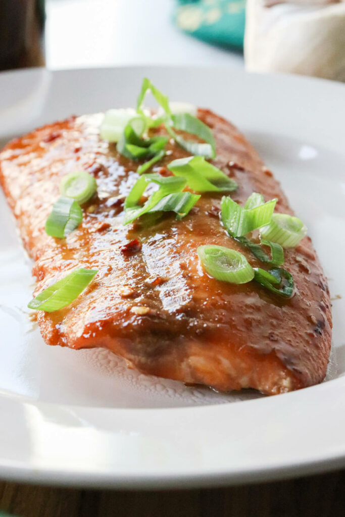 A serving of air fryer teriyaki salmon on a white plate with green onions on top