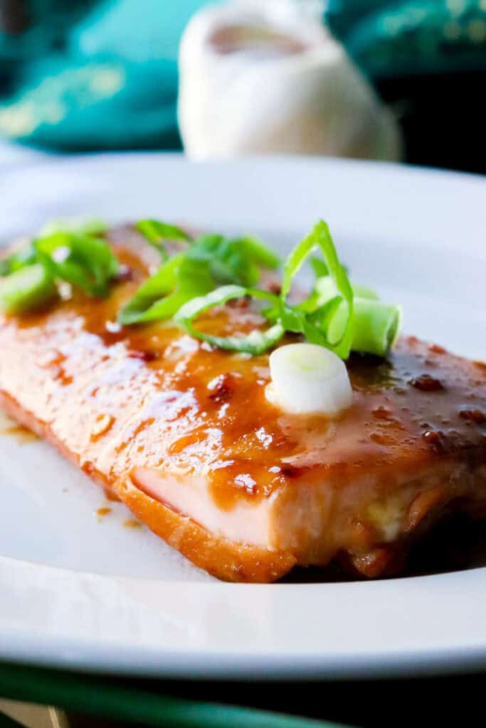 A serving of air fryer teriyaki salmon on a white plate with green onions on top