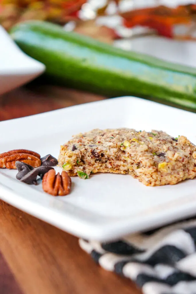 A bite taken out of a keto zucchini chocolate chip cookie on a white square plate