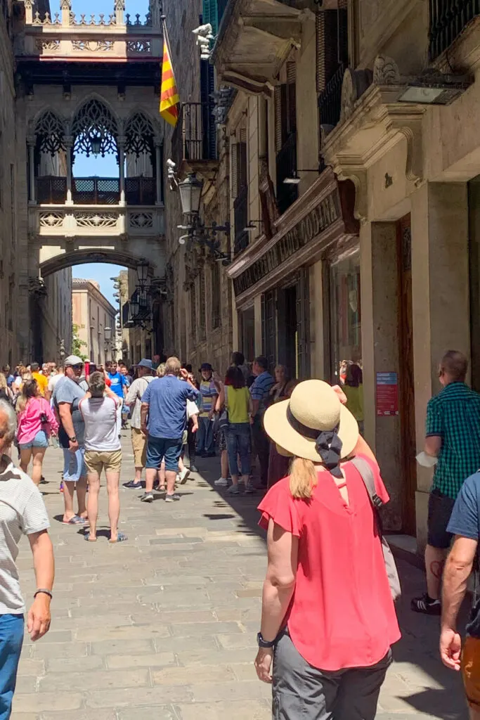Woman in a sunhat and pink shirt looking up a narrow street to the Barcelona Bridge of Sighs
