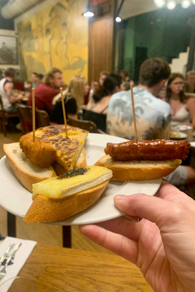 A hand holding up a white plate of 3 tapas