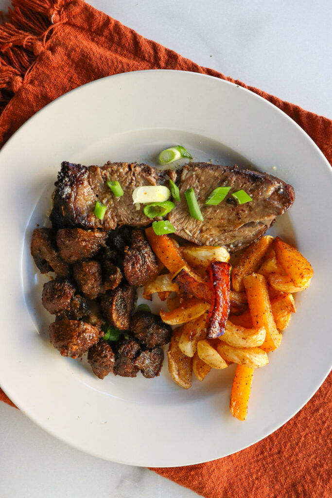 Overhead view of a large slice of air fryer chuck roast on a white plate with fried turnips and mushrooms
