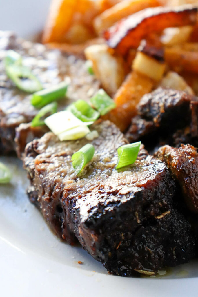 A large slice of air fryer chuck roast on a white plate with fried turnips