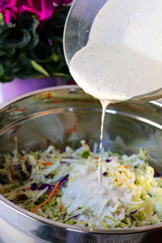 A glass bowl pouring the keto coleslaw dressing into the coleslaw mix