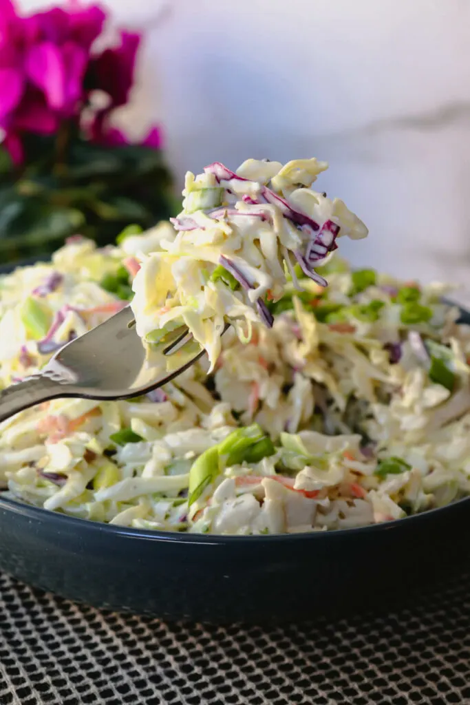 Keto coleslaw bit on a fork held up with magenta flowers in the background