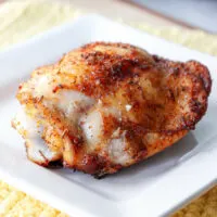 One baked chicken thigh on a white plate