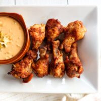 Overhead view of frozen air fryer wings on a white plate with a bowl of green chile queso