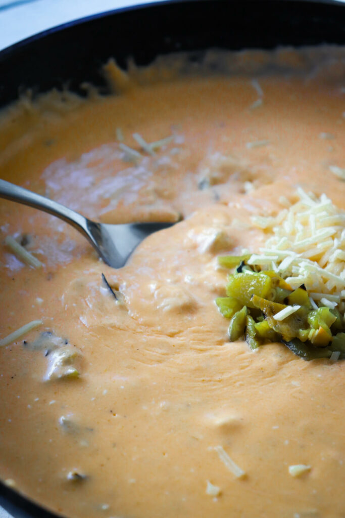 A spoon in a cast iron skillet of green chile cheese dip