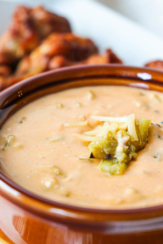 keto queso dip in a brown bowl in front of chicken wings