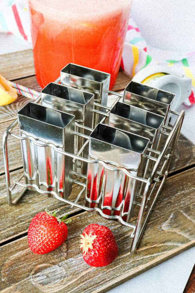 Front view of metal popsicle molds in front of a pitcher of strawberry lemonade