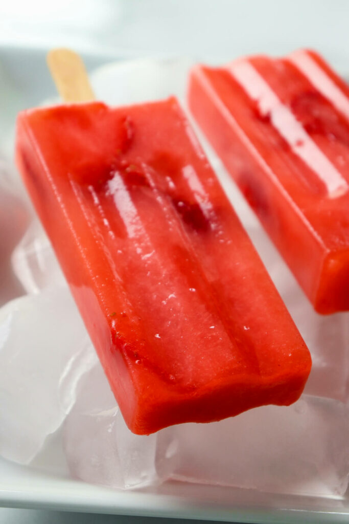 A close up of a view of ared sugar free popsicle, keto strawberry lemonade, on ice