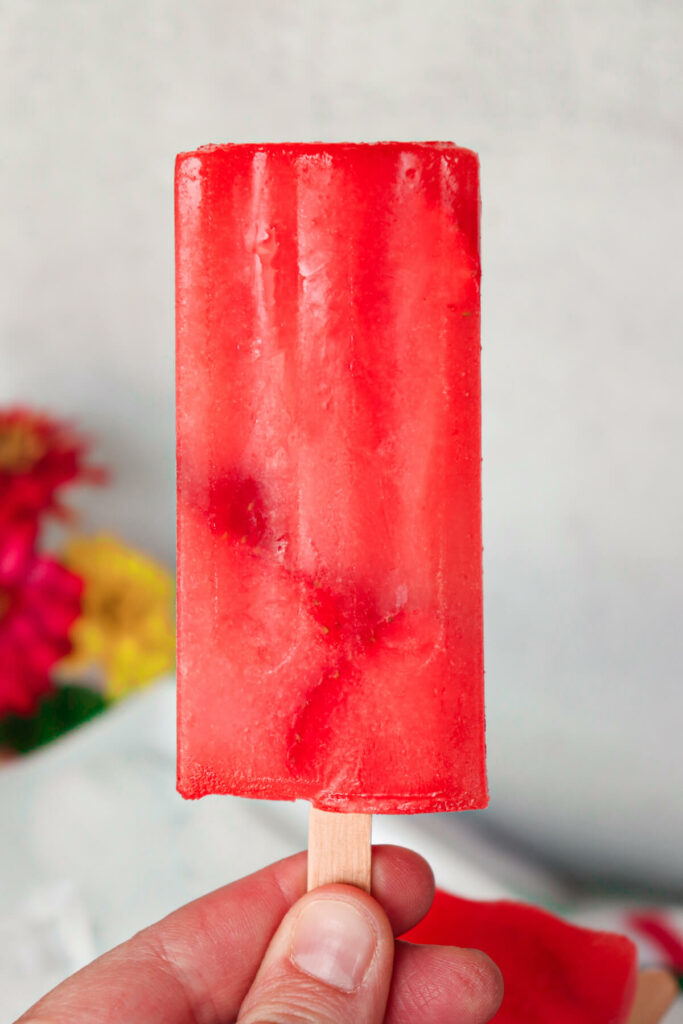 A hand holding up a sugar free strawberry lemonade keto popsicle