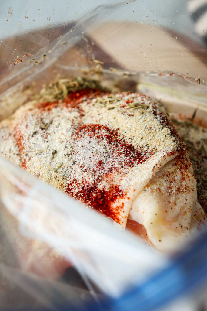 Overhead view of chicken thighs in a zipper bag topped with olive oil and seasoning