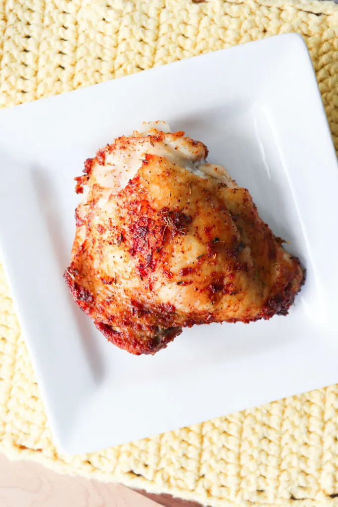 Overhead view of view of an oven baked chicken thigh on a white plate