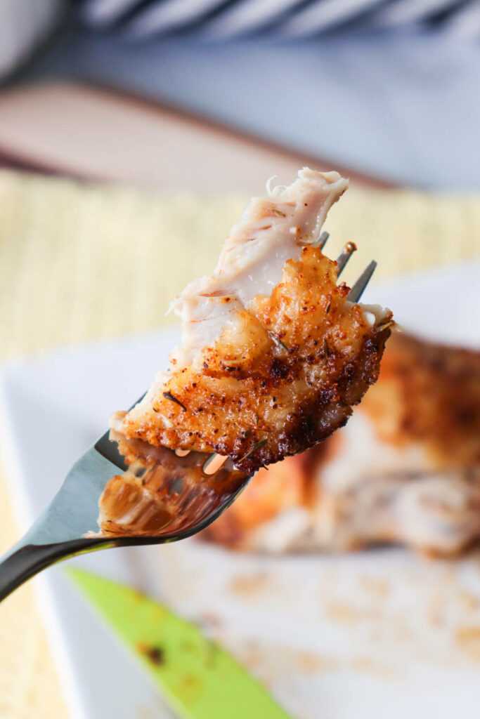 A bite of a chicken thigh on a fork held up in the air