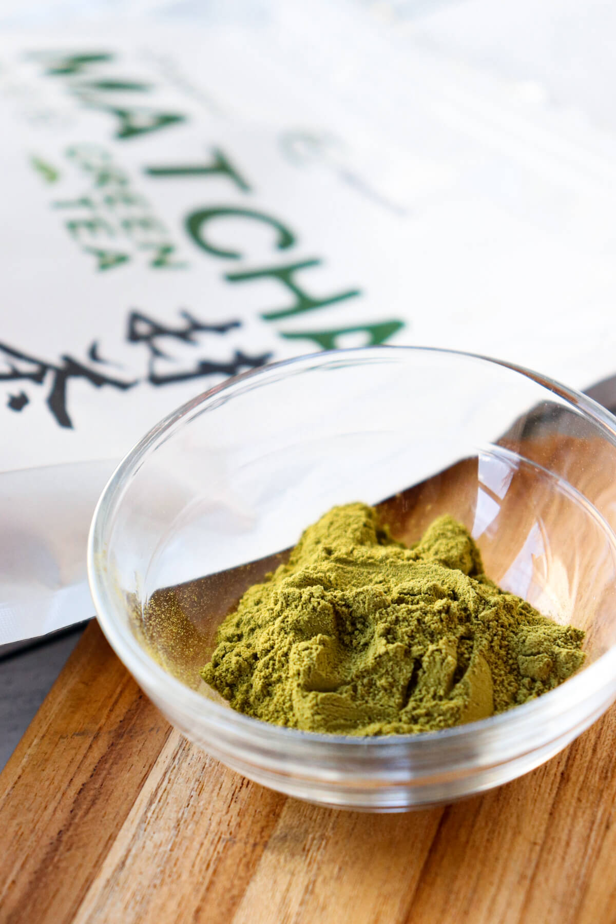 A glass bowl with matcha powder and a bag of it behind