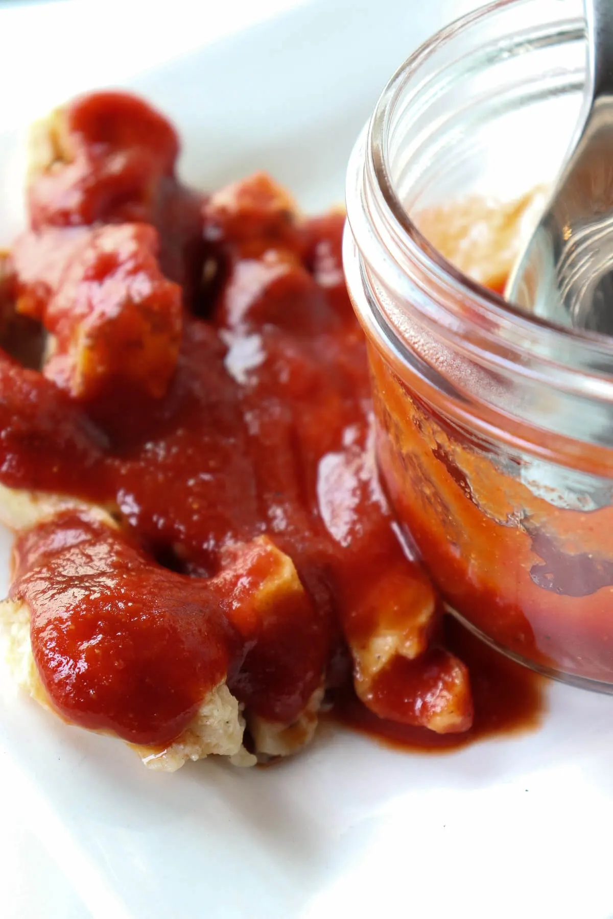 Grilled chicken smothered in sugar free BBQ sauce next to a glass jar