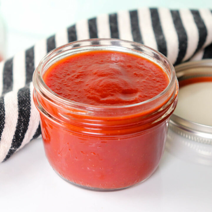 Front view of a glass jar of sugar free ketchup, keto and low carb, with a black and white kitchen towel in the background