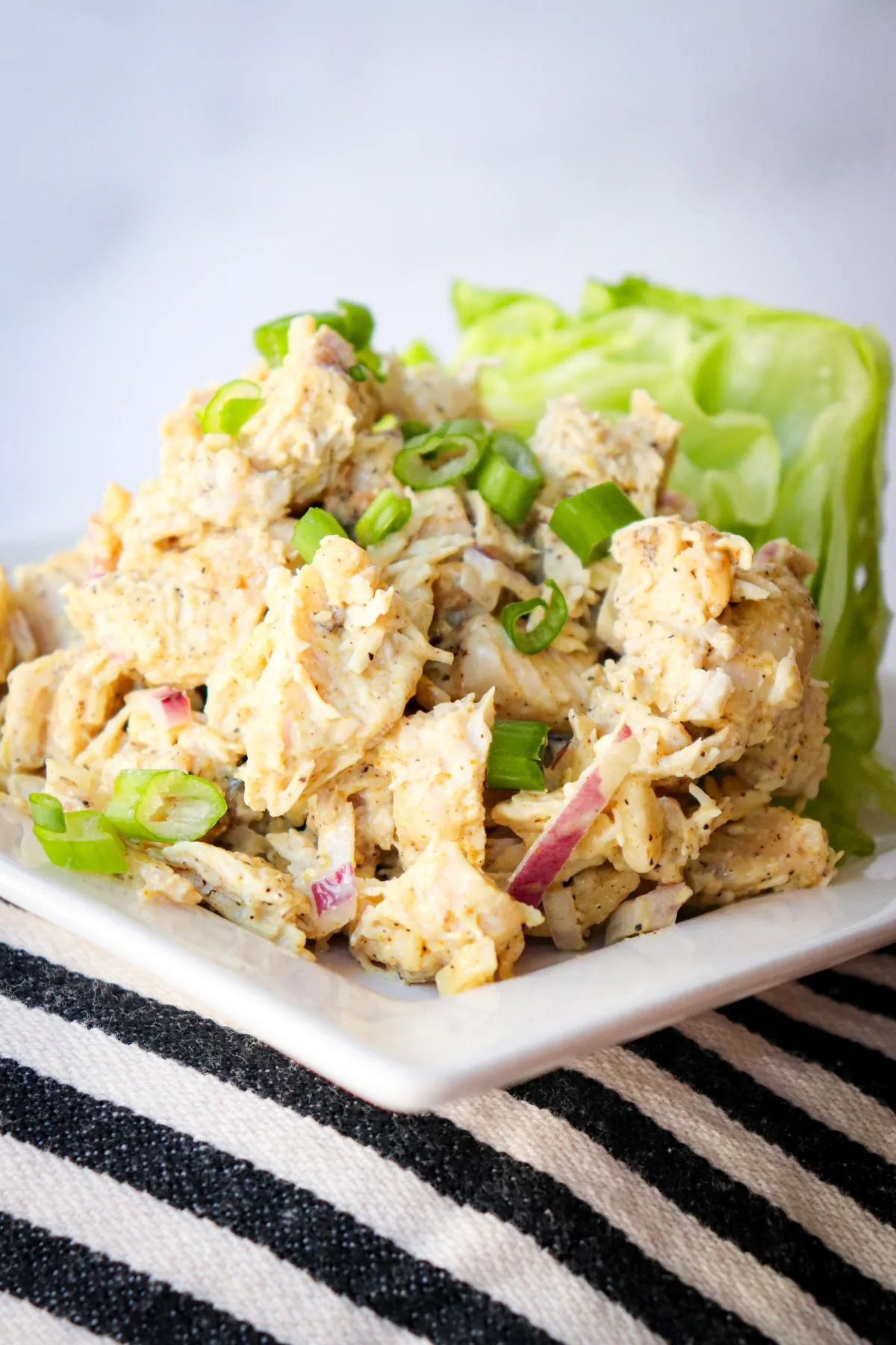 Curry keto chicken salad on a white plate sitting on a black and white striped cloth