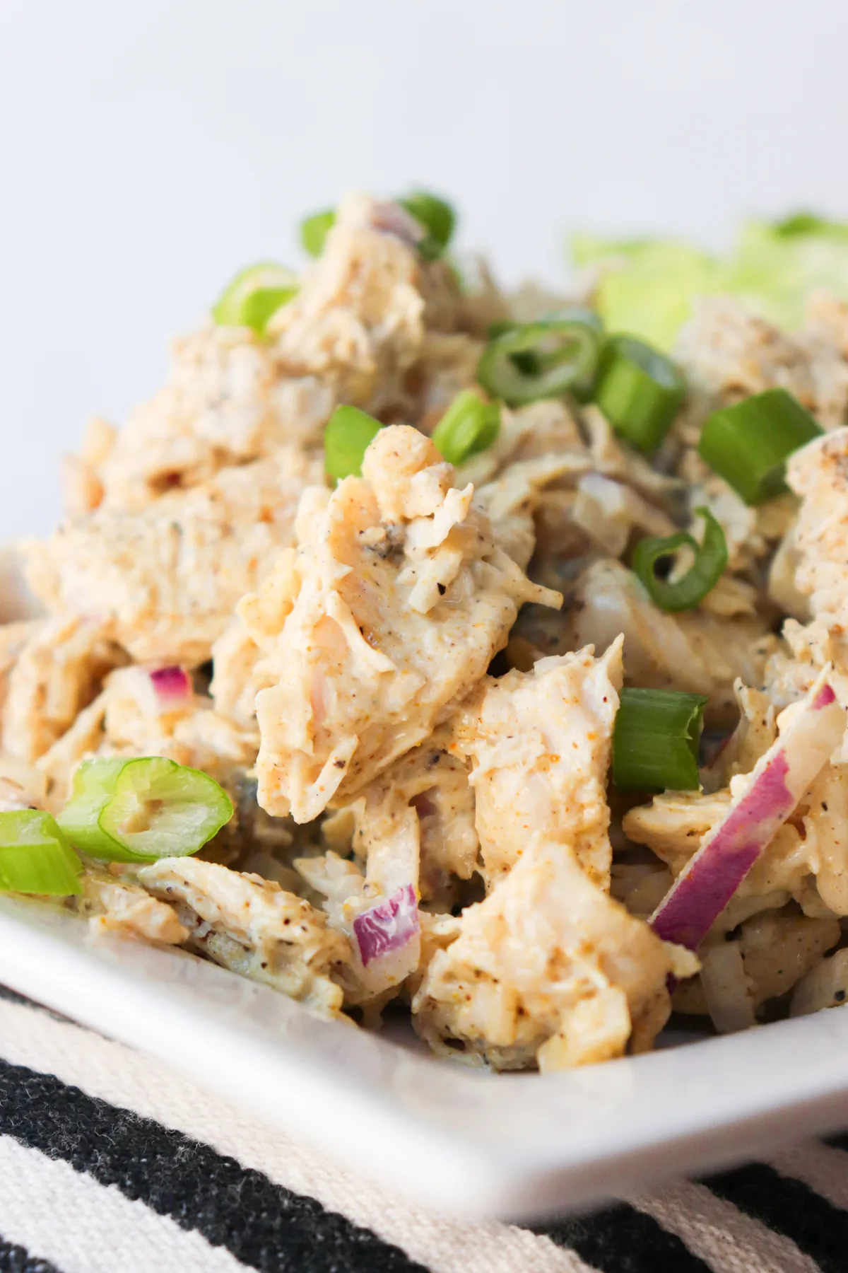 Curry keto chicken salad on a white plate sitting on a black and white striped cloth