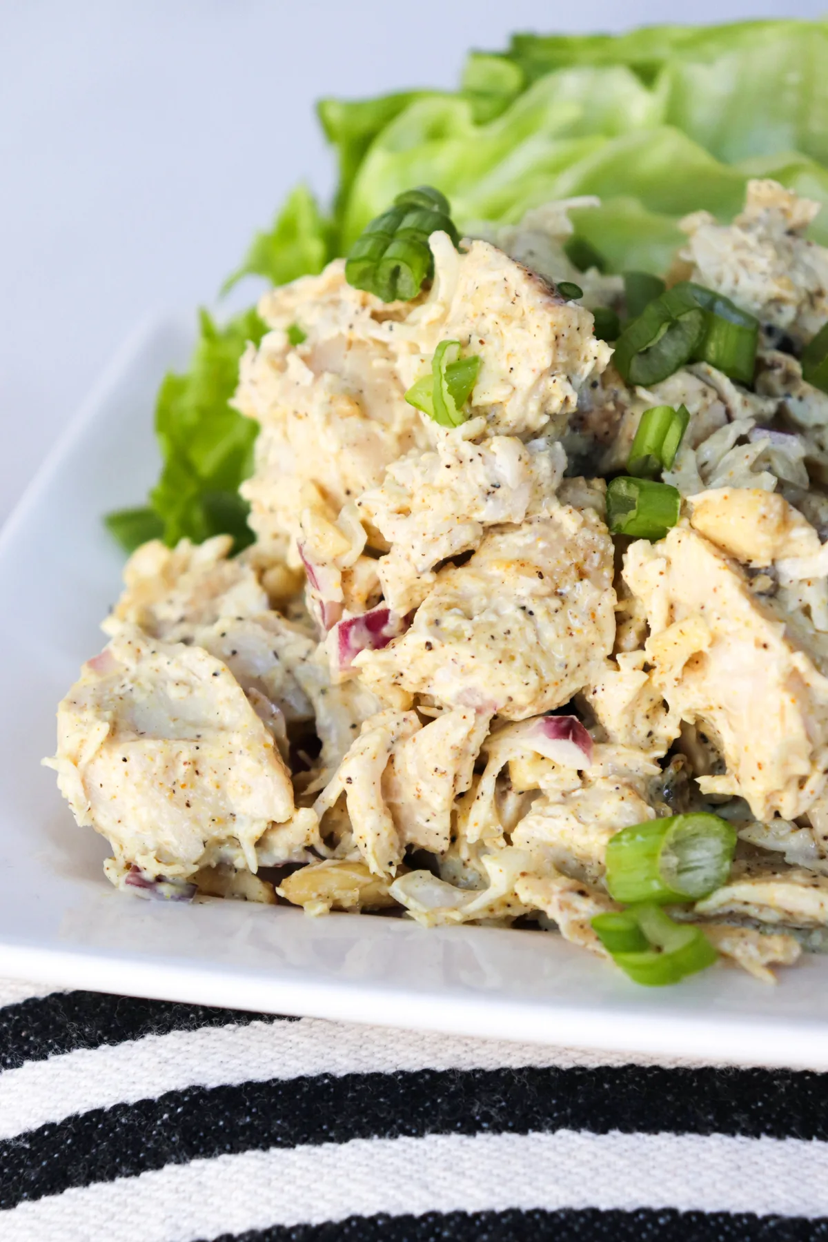 Curry keto chicken salad on a white plate sitting on a black and white striped cloth