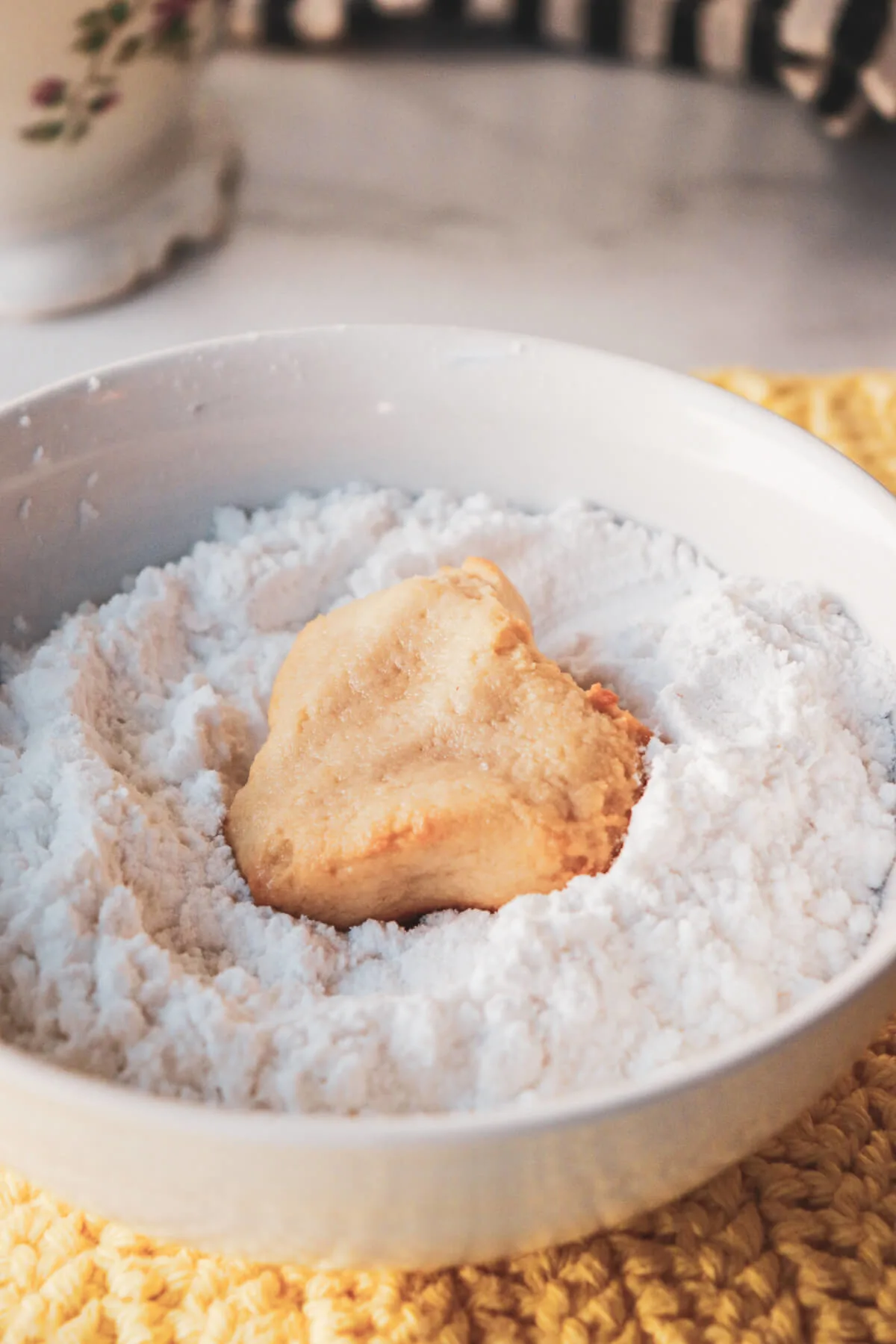 A Greek almond cookie in a bowl of powdered sweetener
