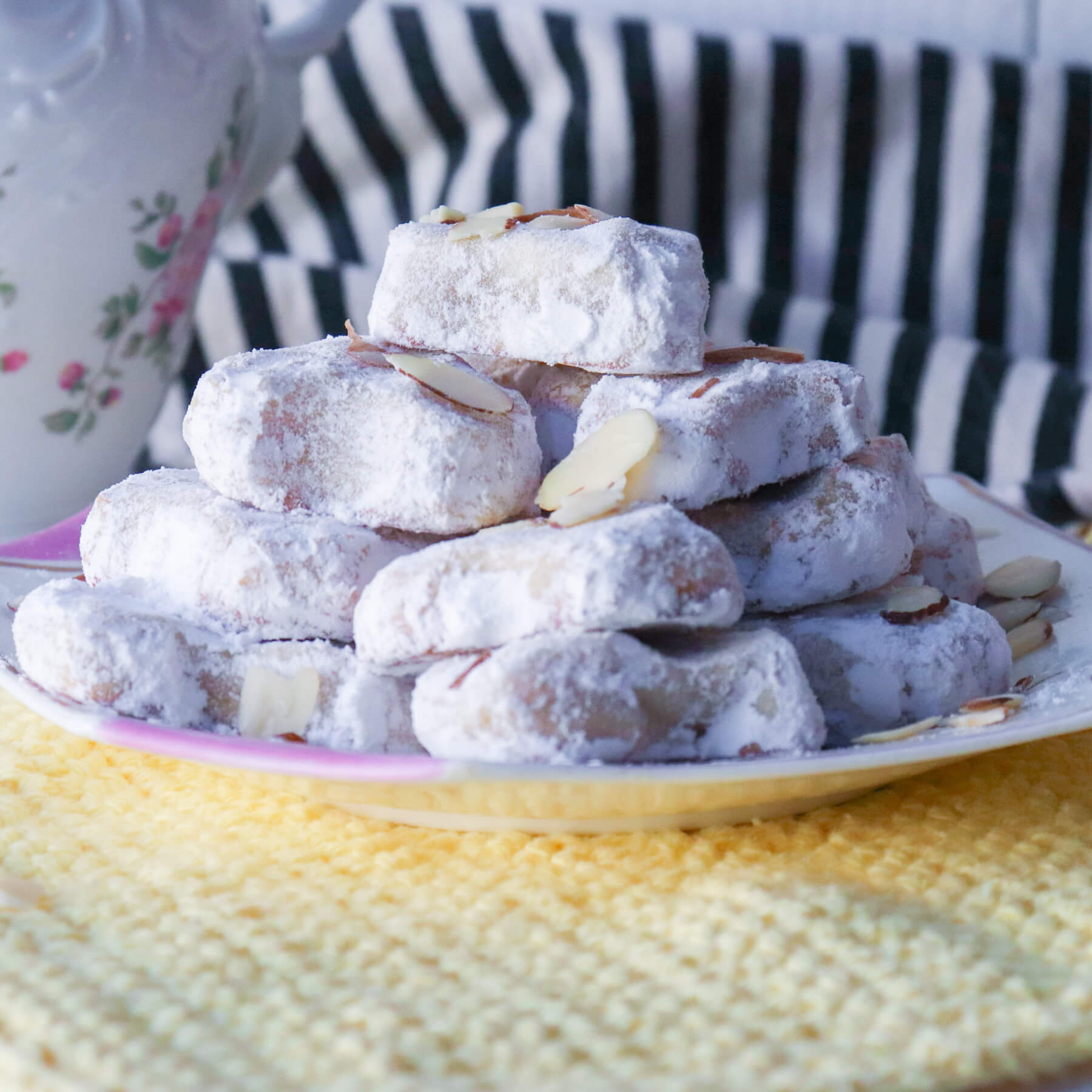 Plate of stacked Greek Almond Cookies, Amygdolata, on a yellow crocheted dishcloth