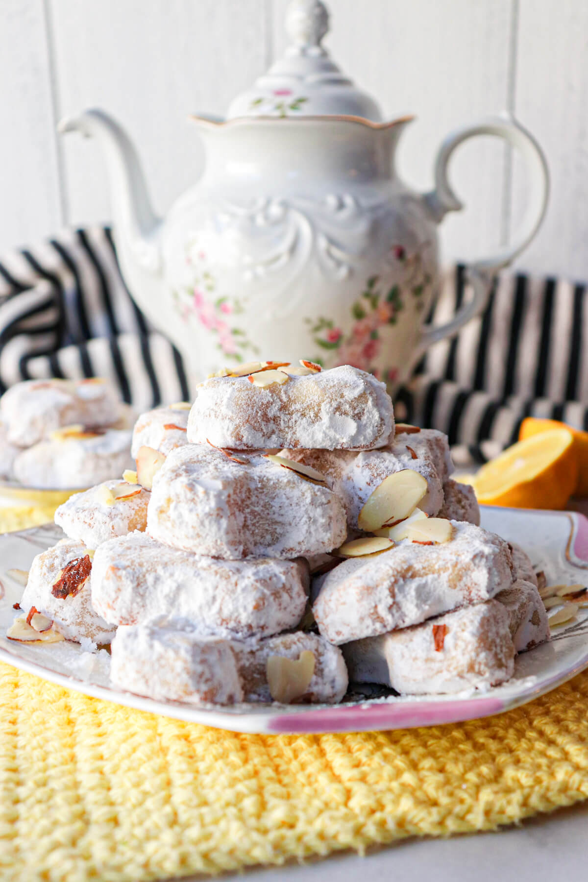 Traditional Greek Almond Cookies in a stack on a white and pink plate with a teapot in the background